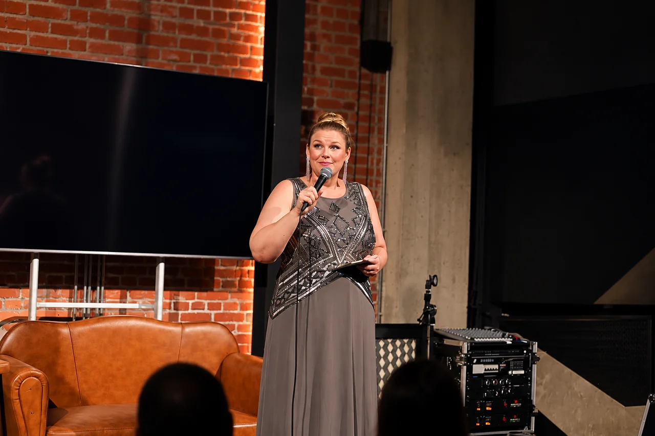 A host holding a microphone on stage at a comedy night