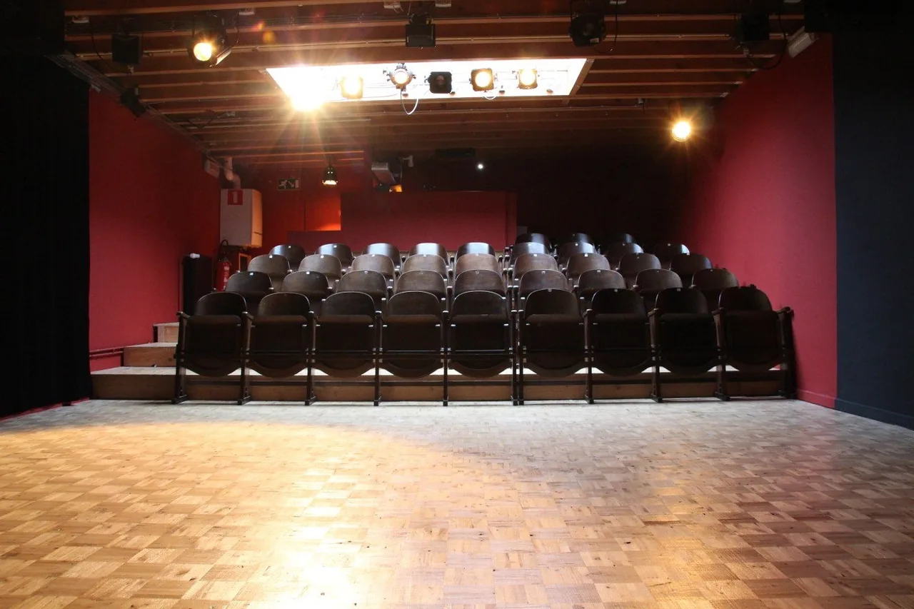 Rows of seats facing the stage in the red-walled Theater Box theatre in Ghent.